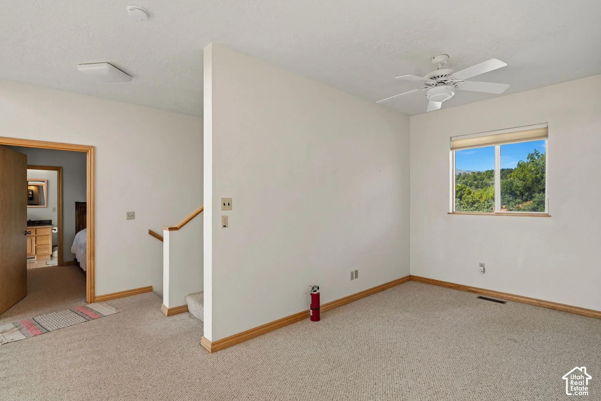 Carpeted flooring, white walls, ceiling fan, and a window with wood trim