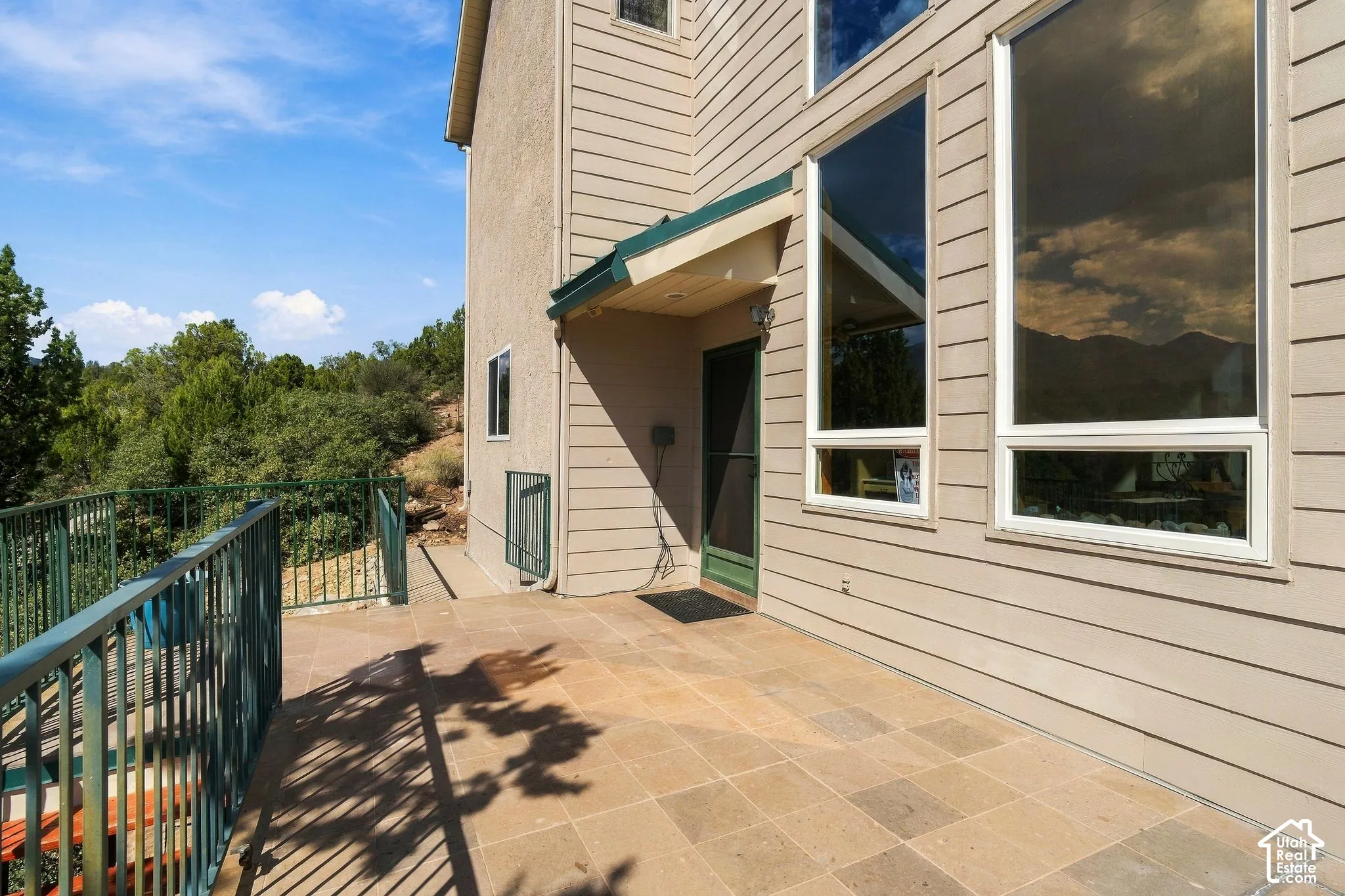Exterior siding, large windows, covered entry, and paved patio with metal railing
