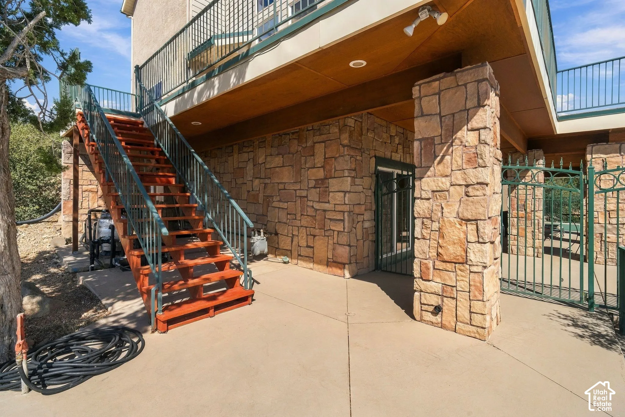 Concrete patio with stone-clad exterior walls, an outdoor staircase with metal railings, and a wrought iron gate