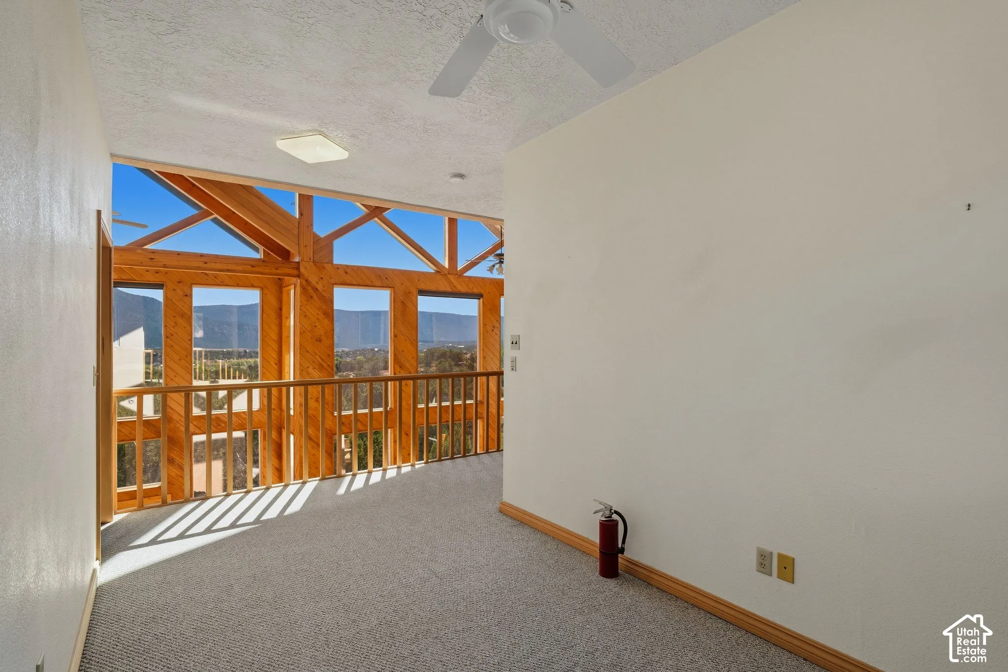 Sunlit room with expansive glass and wood-frame doors opening to an outdoor deck, carpet flooring, and ceiling fan