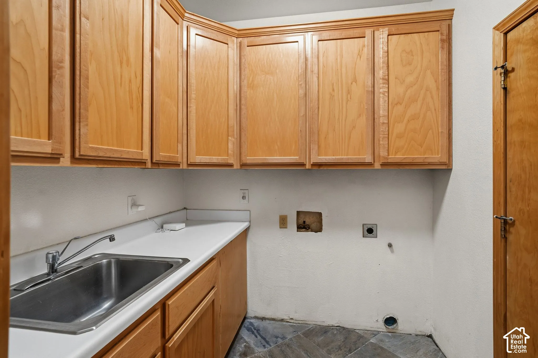 Wood-finish cabinetry, stainless steel sink, chrome faucet, white countertop, and tiled flooring