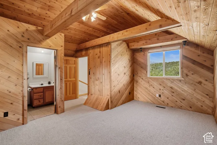 Spacious upper-level bedroom showcasing cathedral ceilings with exposed wood beams, knotty pine walls and ceiling, and generous natural light from a large picture window