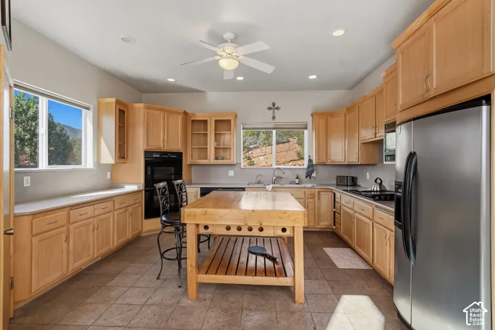 Kitchen featuring extensive wood cabinetry, a central wood-finish island, stainless steel appliances, and tiled flooring