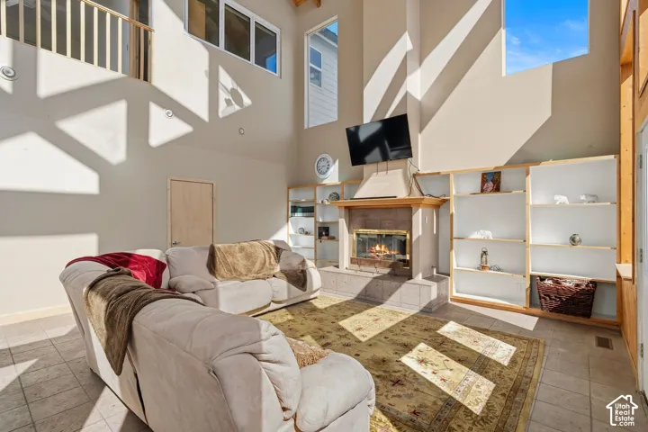 Vaulted ceilings with high windows, a fireplace with a stone surround, built-in shelving, and tile flooring