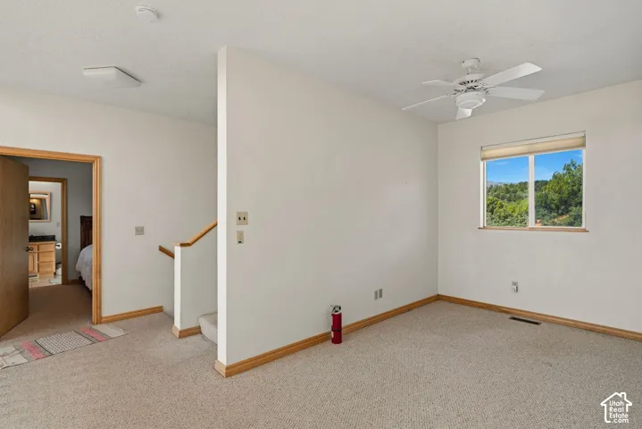 Carpeted flooring, white walls, ceiling fan, and a window with wood trim