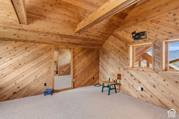 Slanted wood-paneled walls with exposed wooden beams, two framed windows, and light-colored carpeting