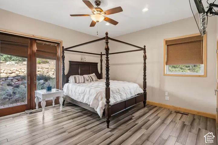 Primary Bedroom Suite featuring a four-poster bed frame, wood-finish flooring with neutral striping, ceiling fan with integrated lighting, and abundant natural light from dual glass doors and transom window