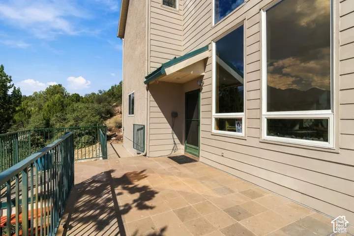 Exterior siding, large windows, covered entry, and paved patio with metal railing