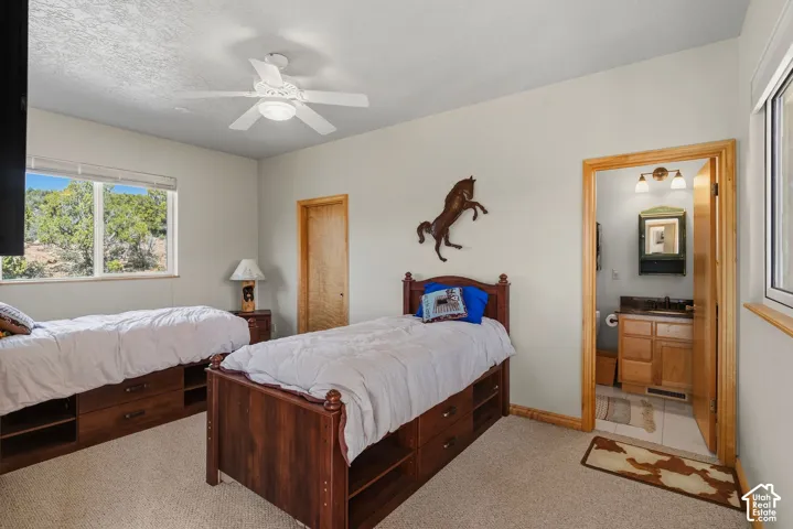 Spacious bedroom featuring dual wood-frame beds with storage drawers, ceiling fan with integrated lighting, wood-trim doorways, and carpet flooring