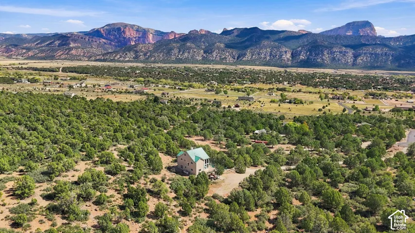 Expansive property featuring abundant mature trees, a multi-story residence with a light-colored exterior and a blue-green roof, set against a backdrop of distant mountains