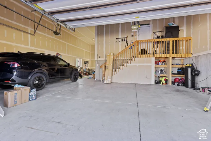 Concrete flooring in a spacious garage featuring a wood staircase with railing, built-in open shelving, and exposed drywall