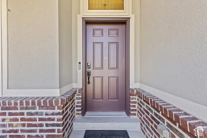Paneled entry door with transom window, stucco exterior, and brick half-walls