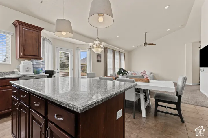 Kitchen island with granite countertop, rich wood-finish cabinetry, and pendant lighting