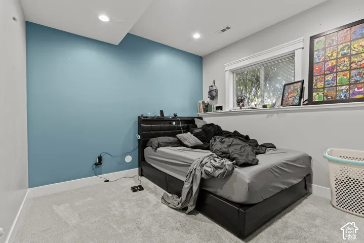 Recessed ceiling lighting, light gray wall paint, contrasting accent wall, window with white trim, and light-colored carpet flooring