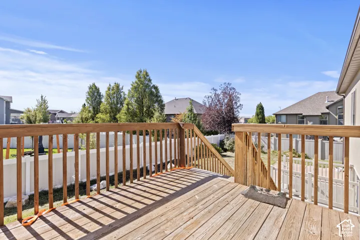 Spacious wood deck with natural wood railing and stairs, overlooking a fenced backyard
