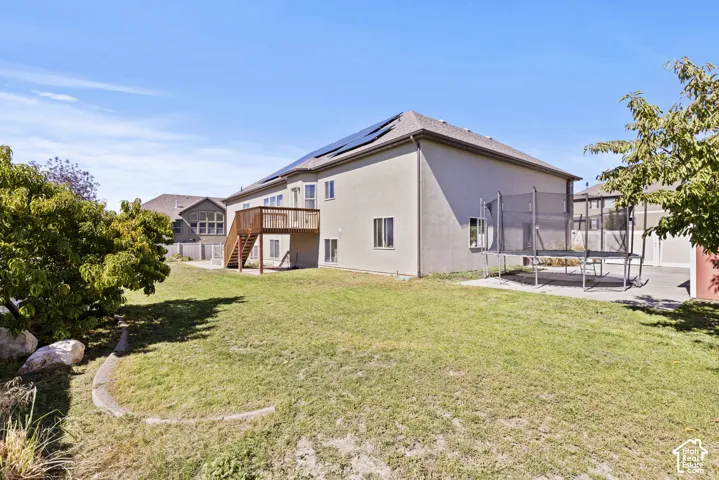 Expansive backyard featuring a stucco exterior, upper-level wood deck, ground-level patio, and solar panels