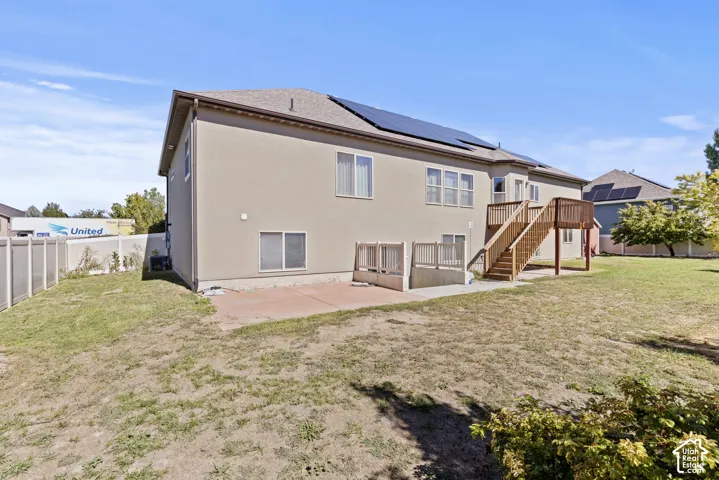 Exterior stucco finish, visible solar panels, ground-level patio, upper-level wood deck, and wood privacy fencing