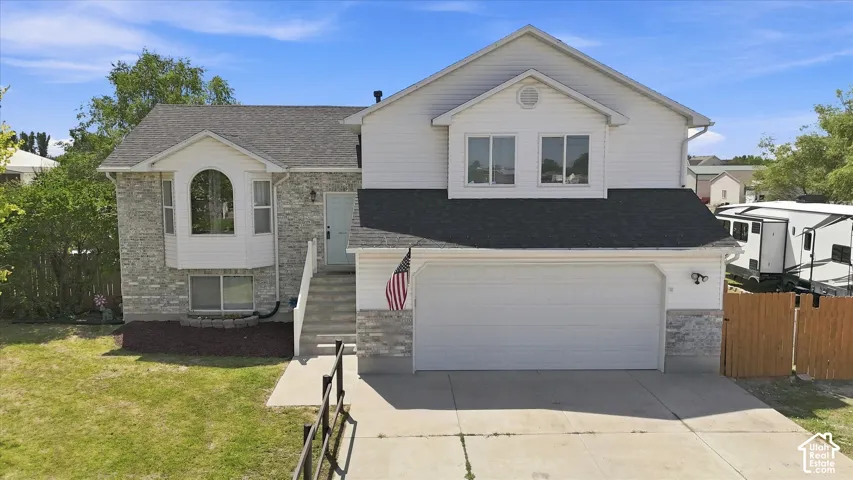 Two-story residence featuring a stone and vinyl exterior with a prominent front-facing gable, two-car garage with paneled door, circular entry vestibule with arched doorway, manicured front lawn with mature landscaping, and an American flag mounted at the