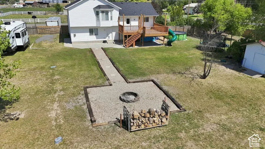Expansive yard featuring a gravel fire pit area with timber edging, a raised wood-finish deck with stairs, and a white exterior storage shed