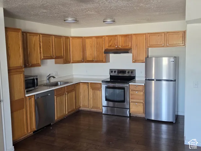 Kitchen featuring wood cabinetry, stainless steel appliances, a corner sink with a high-arc faucet, and dark wood-finish flooring