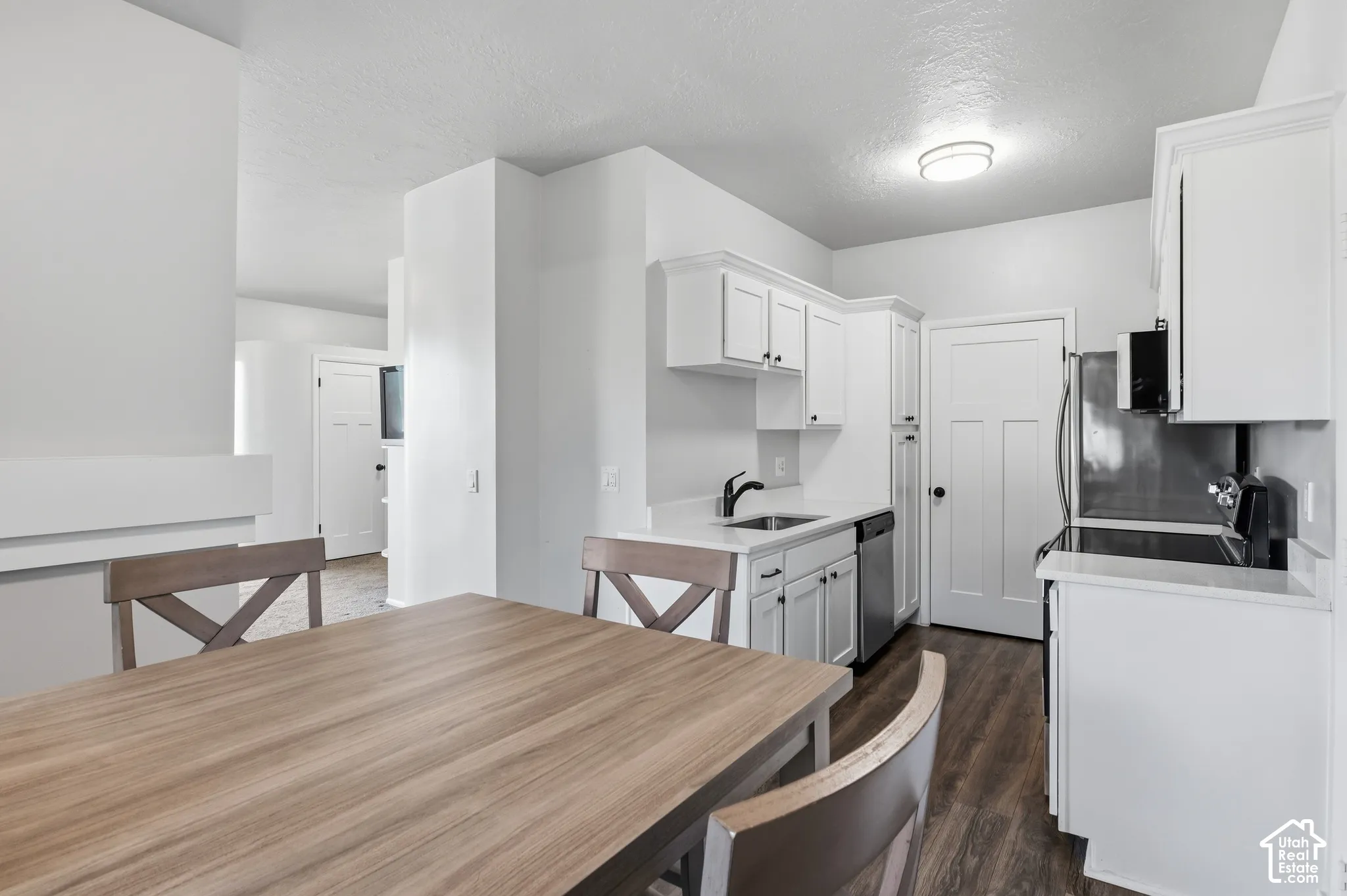 Open-concept kitchen and dining area featuring white cabinetry, stainless steel appliances, wood-finish flooring, and a spacious dining table with seating for multiple guests