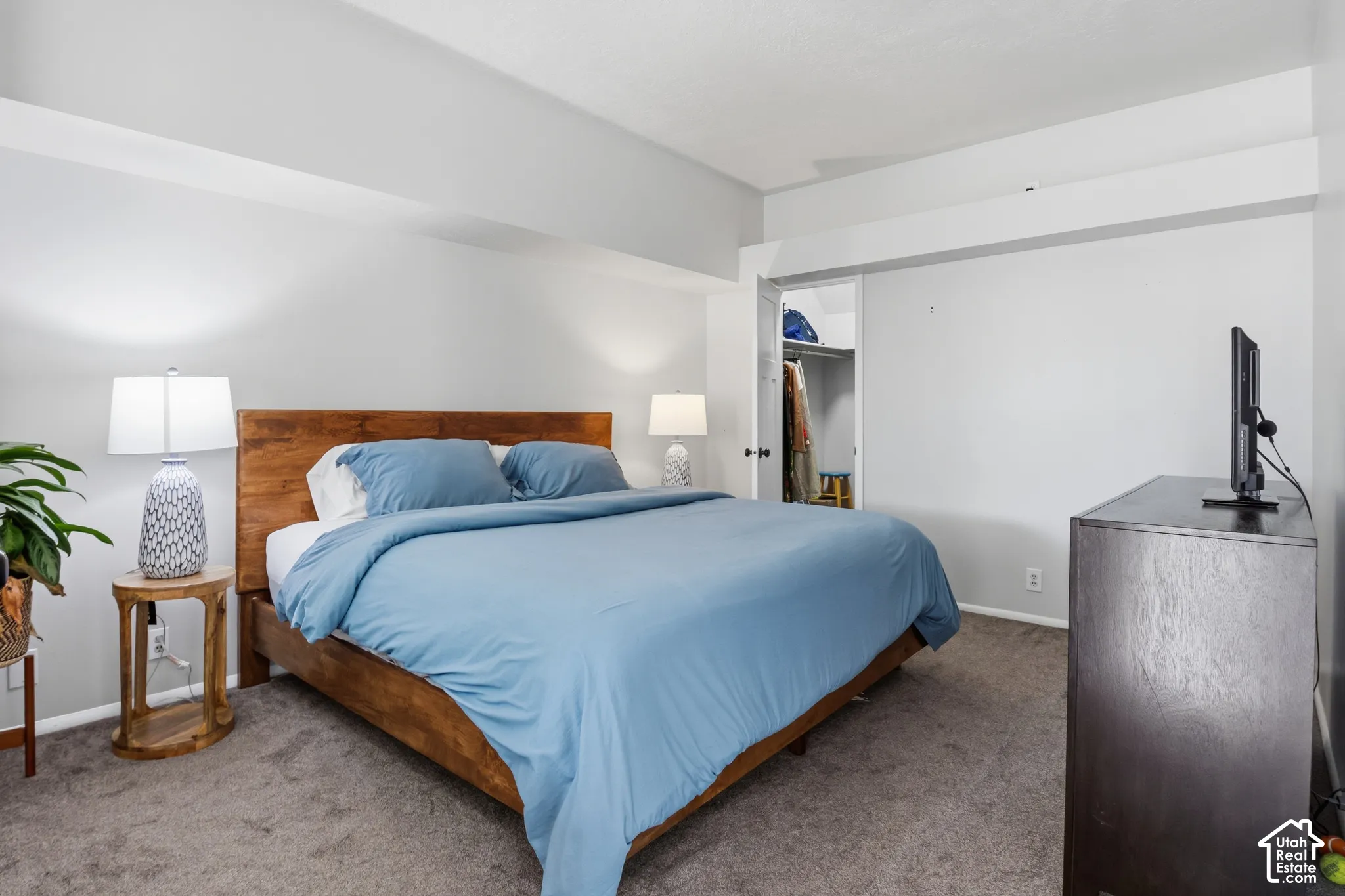 Spacious primary bedroom featuring a wood-finish bed frame, soft blue bedding, carpeted flooring, and abundant natural lighting from multiple windows
