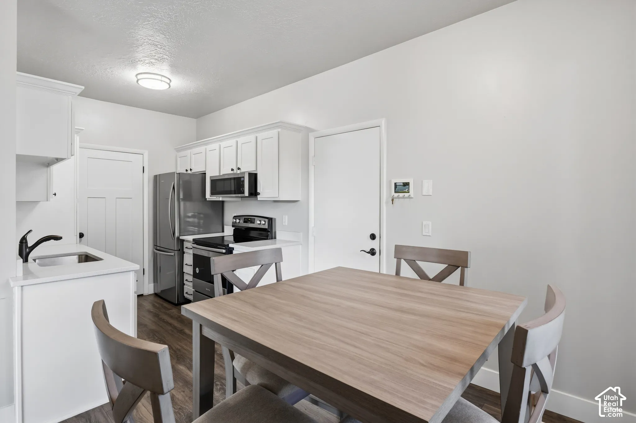 White cabinetry with crown molding, stainless steel appliances, wood-finish flooring, and white countertops