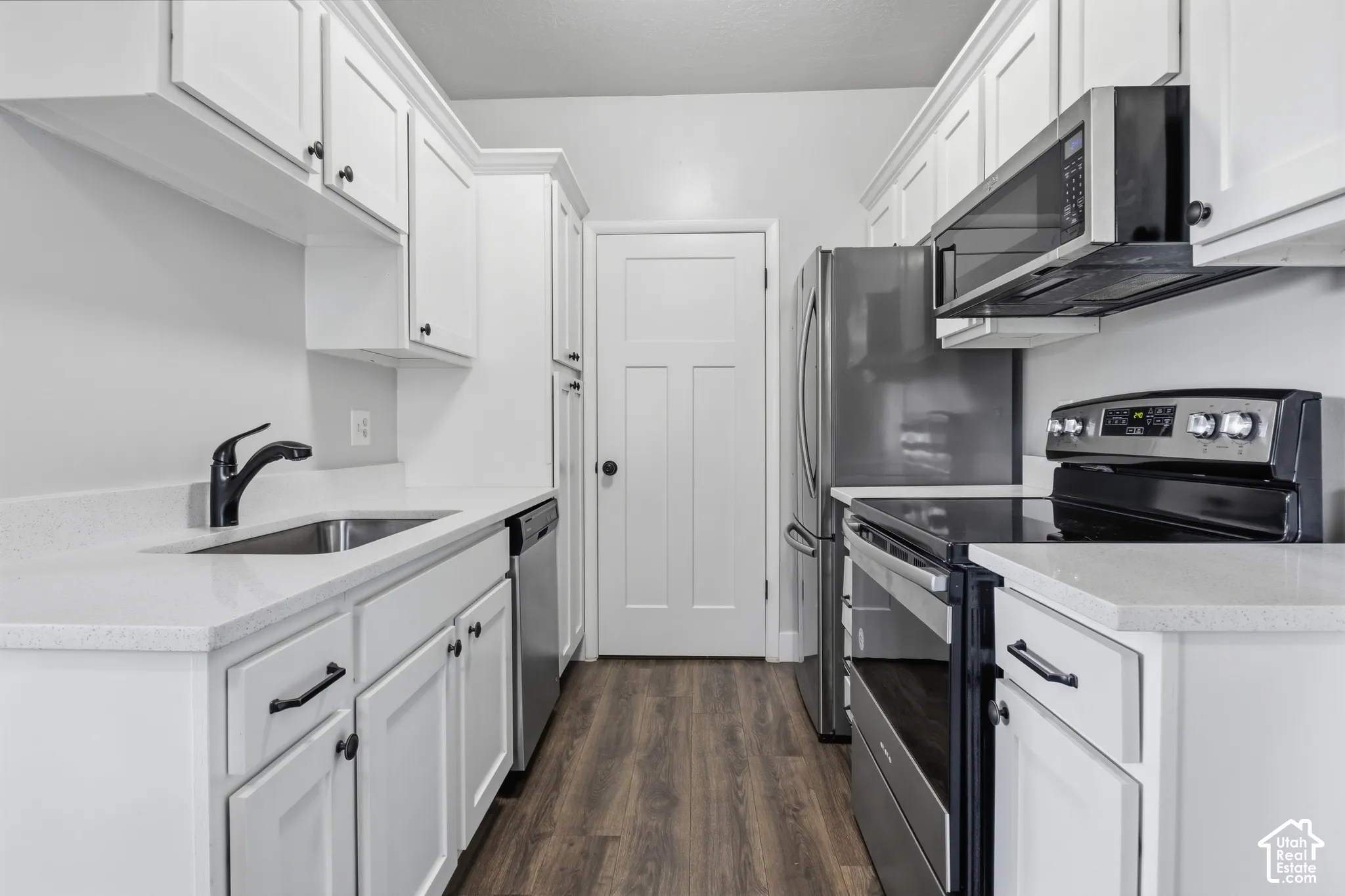 White cabinetry with dark hardware, stainless steel appliances, light-toned countertops, and wood-finish flooring