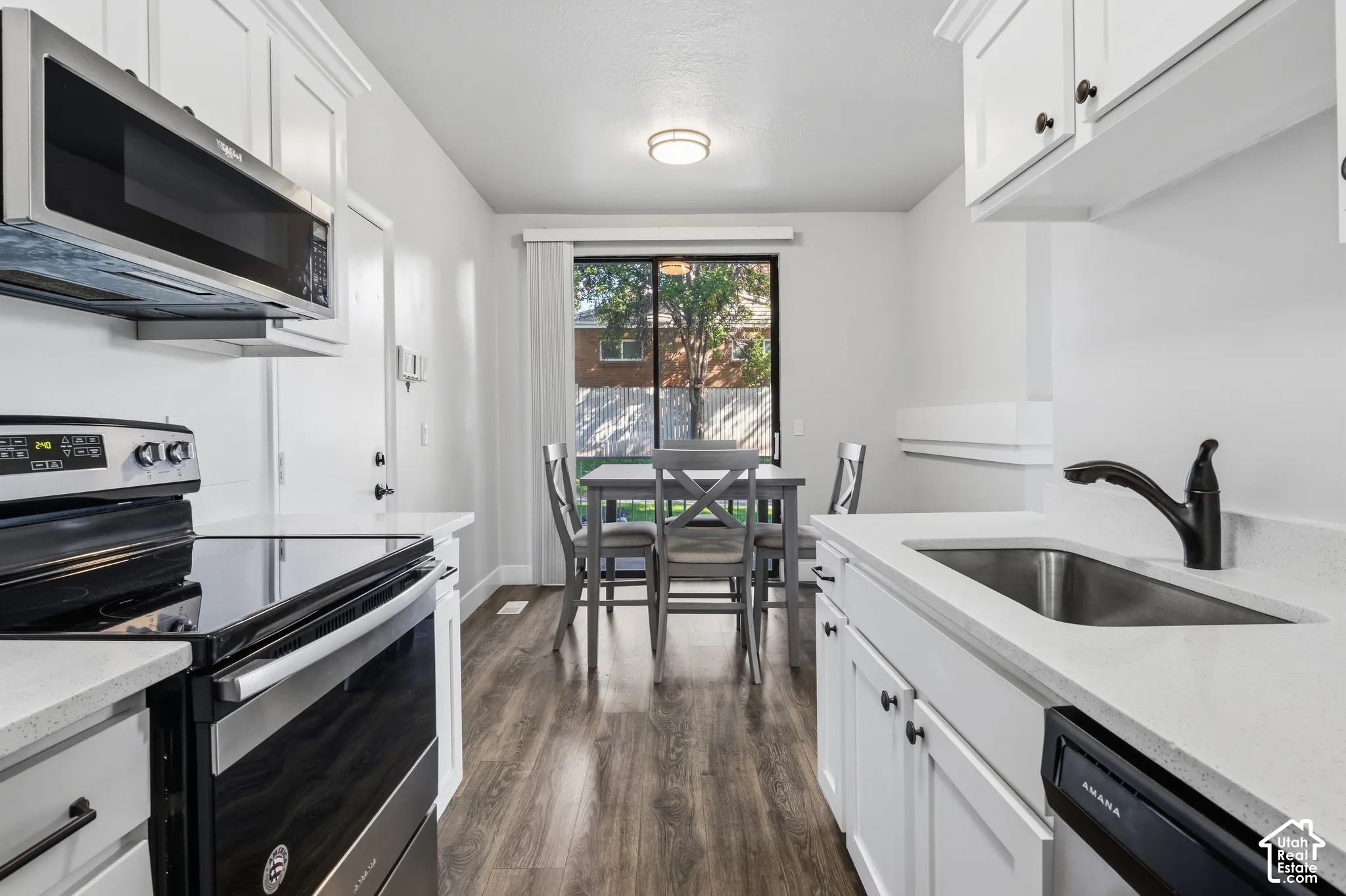 White cabinetry with matte black hardware, stainless steel appliances, light-toned countertops, wood-finish flooring, and a sliding glass door