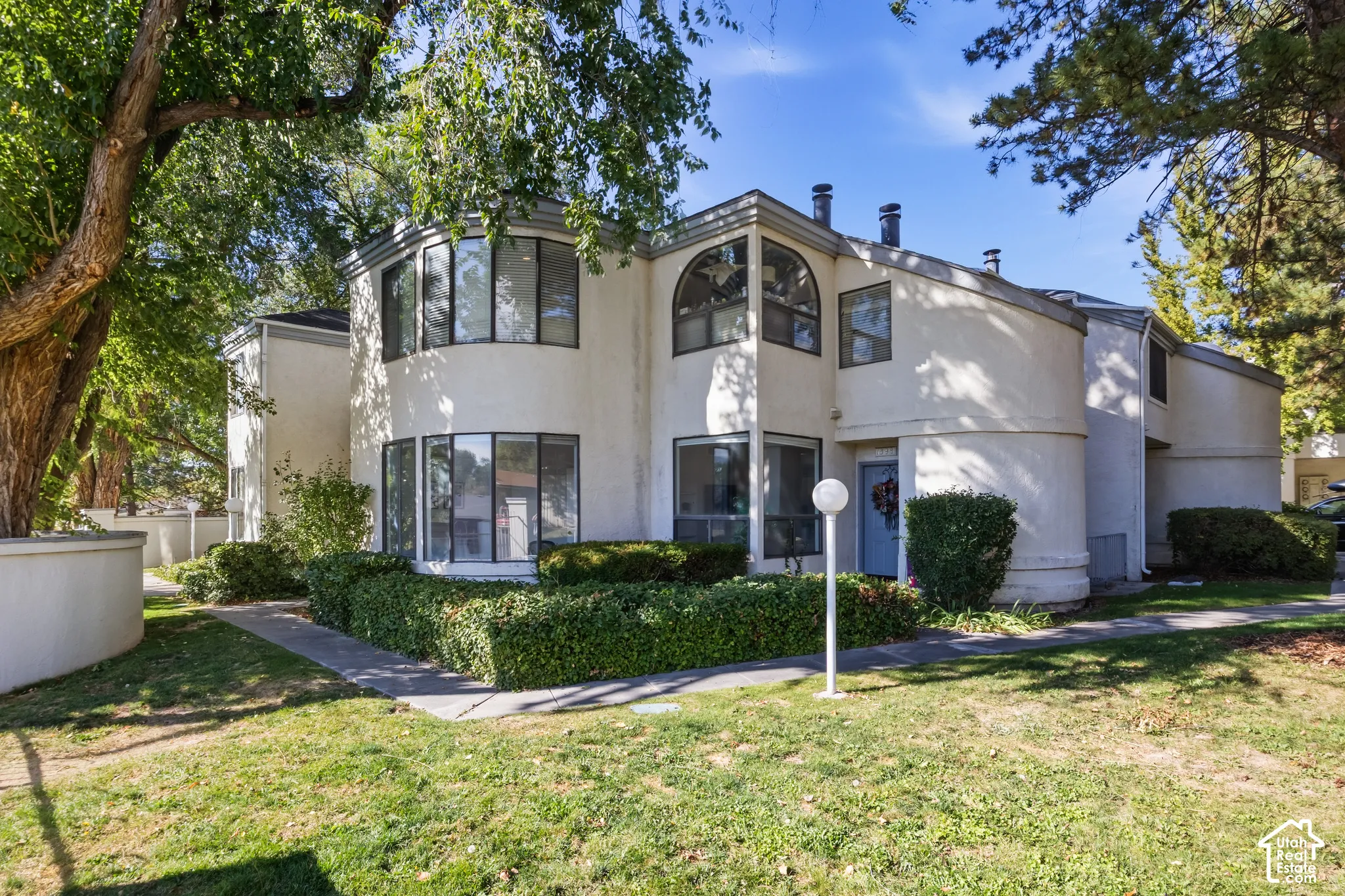 Stucco exterior with multiple bay windows, mature trees, and established landscaping