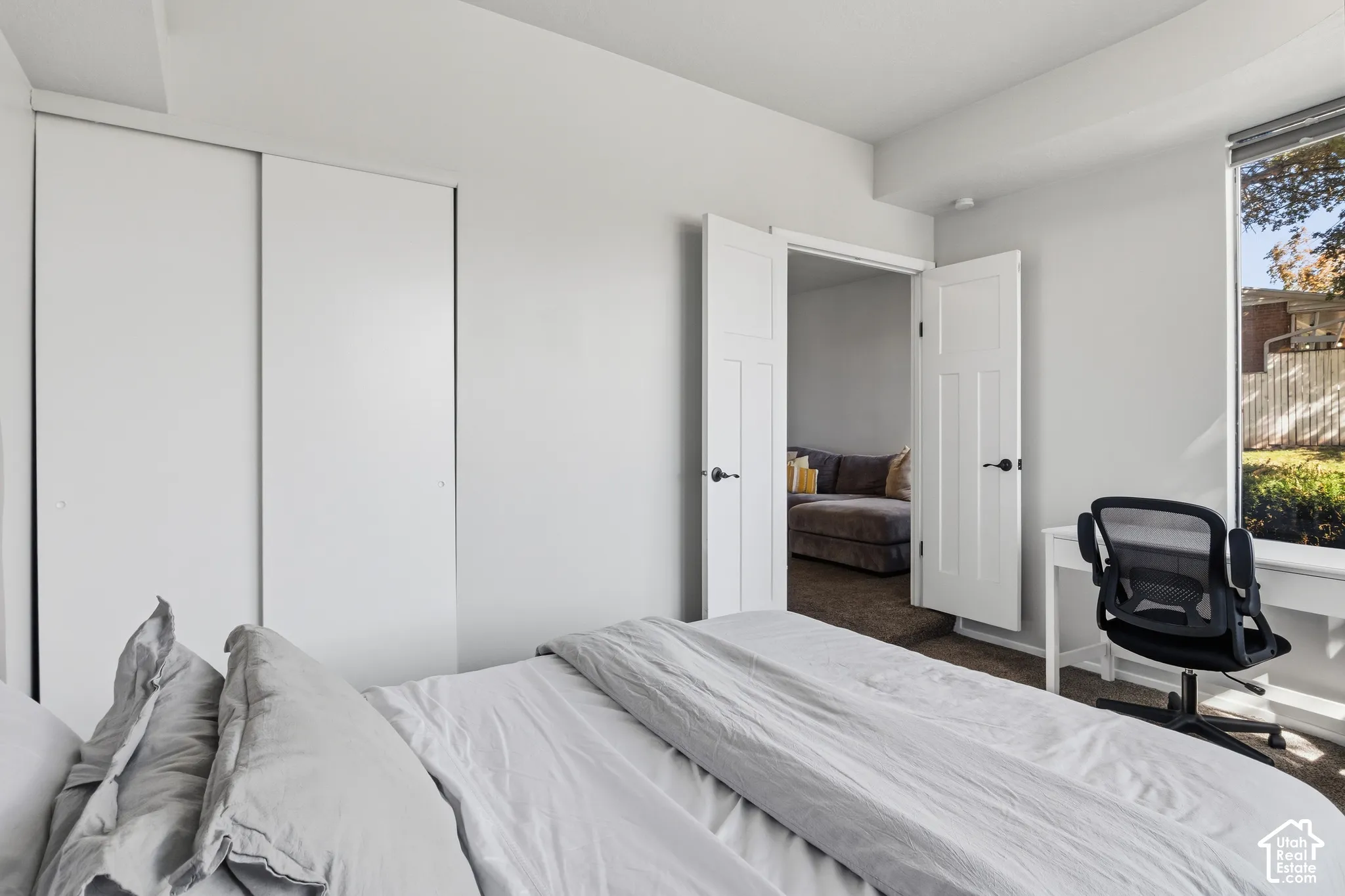 Bright, light-filled bedroom featuring expansive white sliding closet doors, multiple entry points with white panel doors, and large windows framing natural outdoor scenery