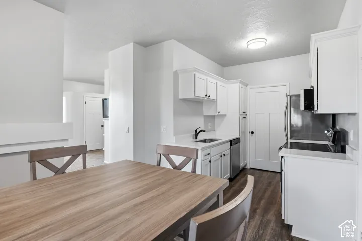 Open-concept kitchen and dining area featuring white cabinetry, stainless steel appliances, wood-finish flooring, and a spacious dining table with seating for multiple guests