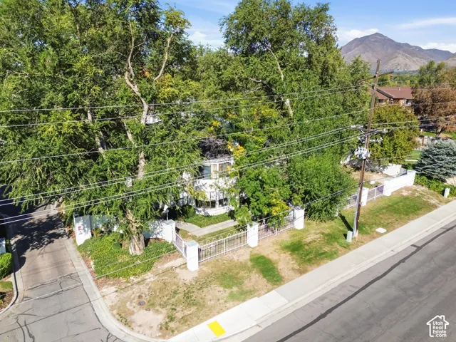 Gated property entrance with a white perimeter fence, mature trees, and a mountain backdrop