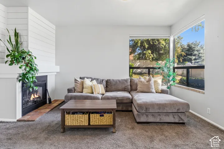 Living area with carpet flooring, a corner fireplace featuring shiplap detailing and a hearth, and dual large windows providing natural light
