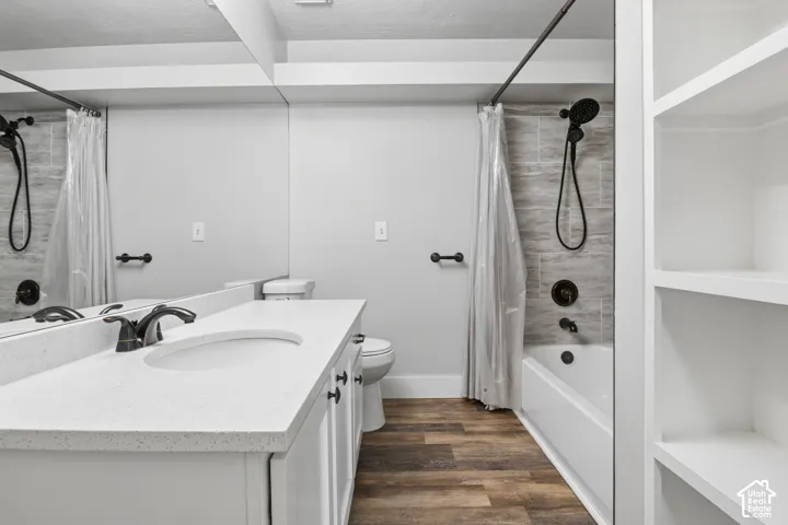 White vanity with an integrated basin and dark bronze fixtures, quartz countertop, wood-finish flooring, built-in shelving, and a tiled shower-bath combination