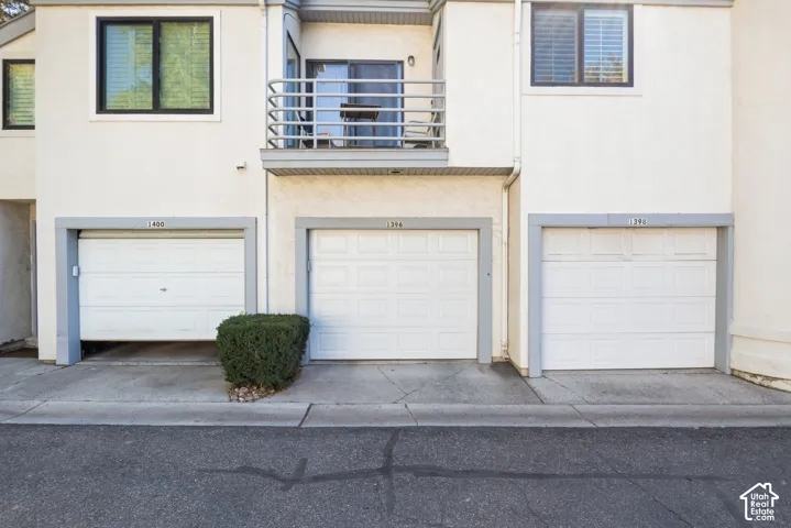 Garage Level Featuring Three Individual White Paneled Garage Doors with Metal Framing, Concrete Driveway, and Modern Multi-Unit Residential Architecture with Stainless Steel Railings on Upper Balcony