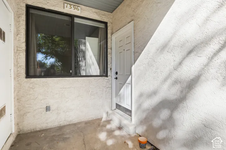 Textured stucco exterior with a paneled entry door, black window framing, and a concrete patio