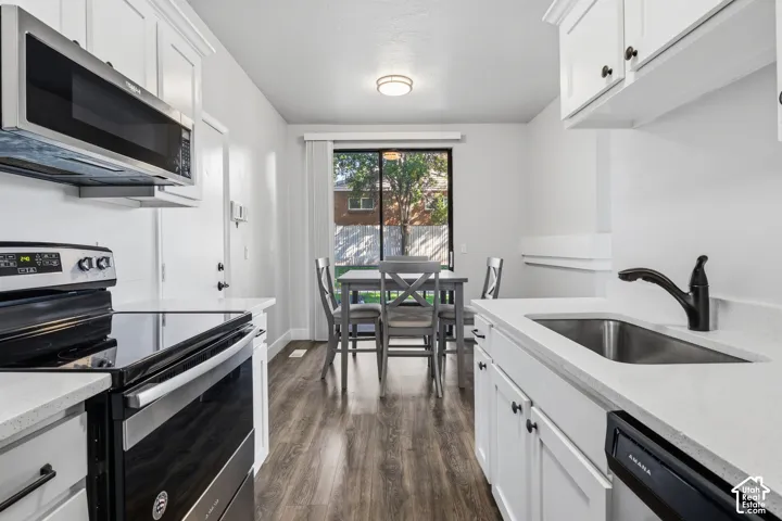White cabinetry with matte black hardware, stainless steel appliances, light-toned countertops, wood-finish flooring, and a sliding glass door