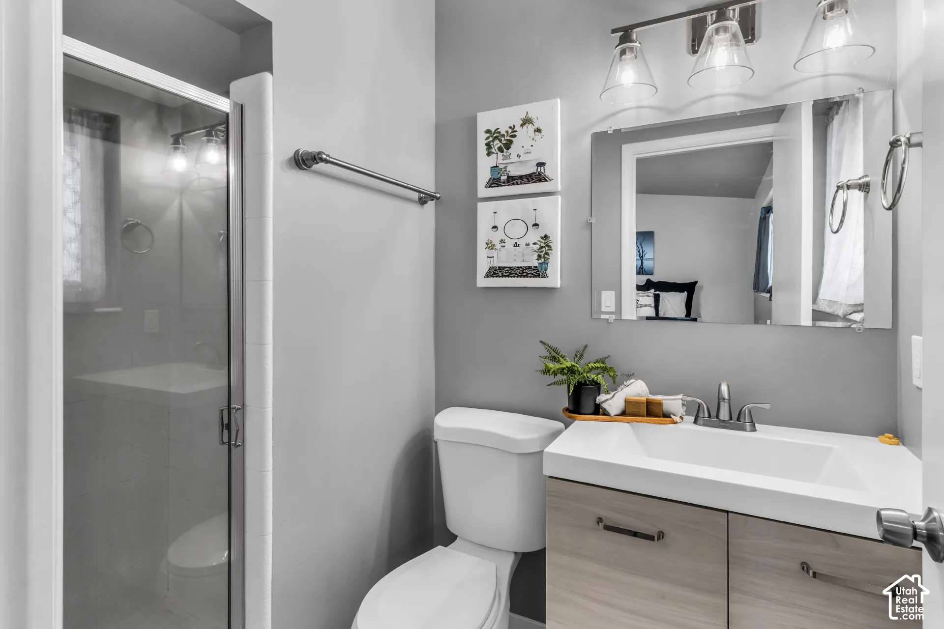 Glass-enclosed shower, single vanity with wood-finish cabinetry, rectangular undermount sink, wall-mounted light fixture, and a large mirror