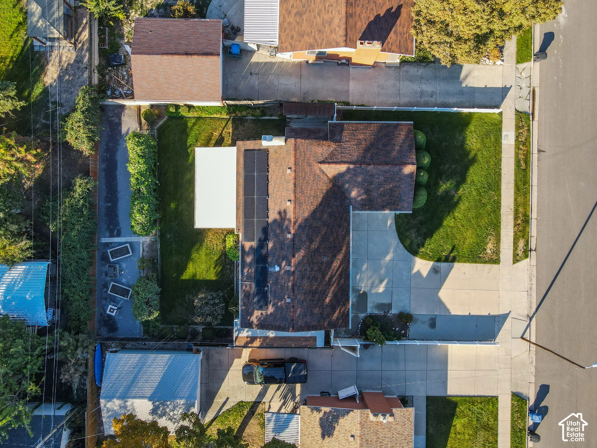 Pitched roof main residence with solar panels, mature landscaping, and a concrete driveway