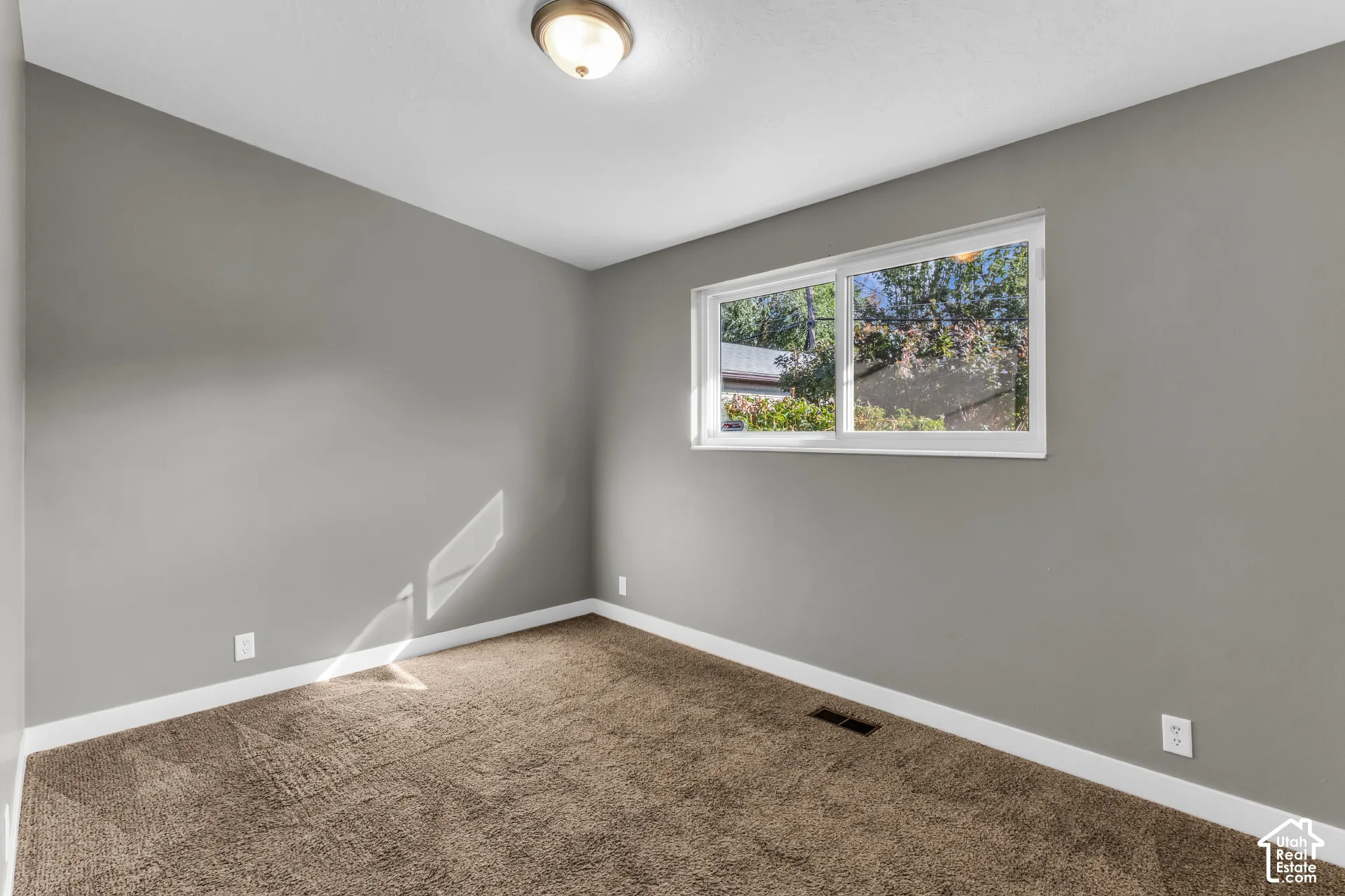 Bright corner bedroom featuring neutral gray walls, soft white ceiling trim, and neutral-toned carpet flooring