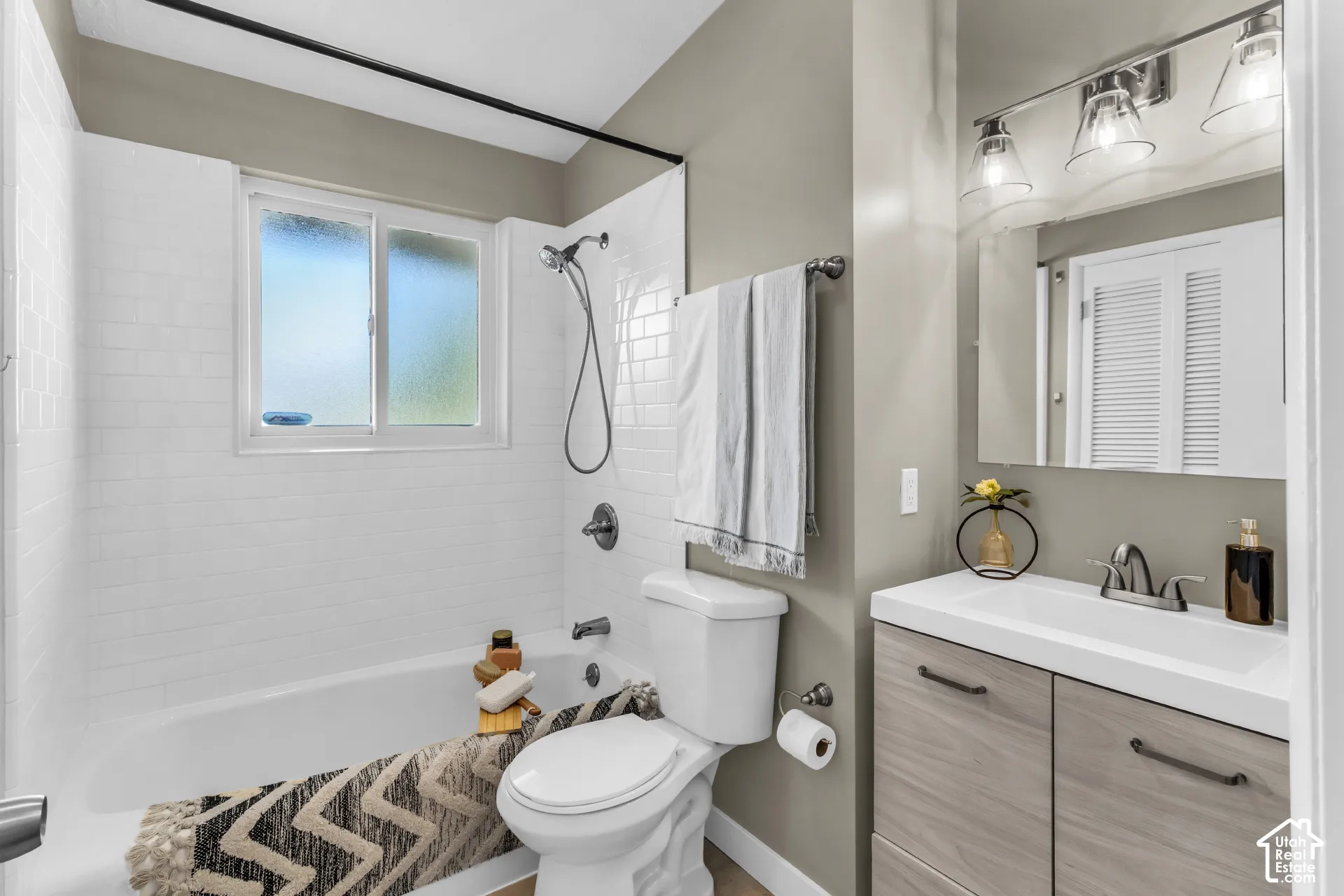 Main bathroom with a Laundry Chute! White subway tile shower surround with a window, single vanity with wood-finish cabinetry, and a chrome-finish faucet