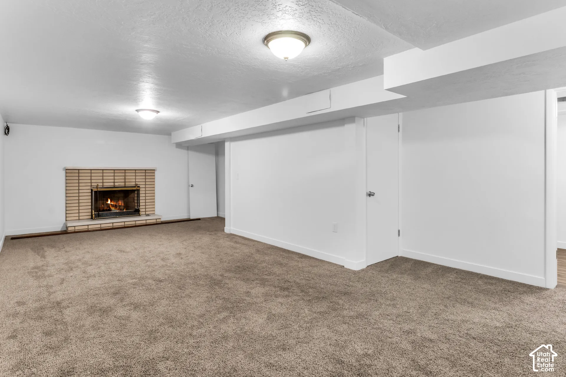 Spacious basement recreation area featuring neutral carpet flooring, recessed ceiling lighting, and a brick fireplace with wood mantel