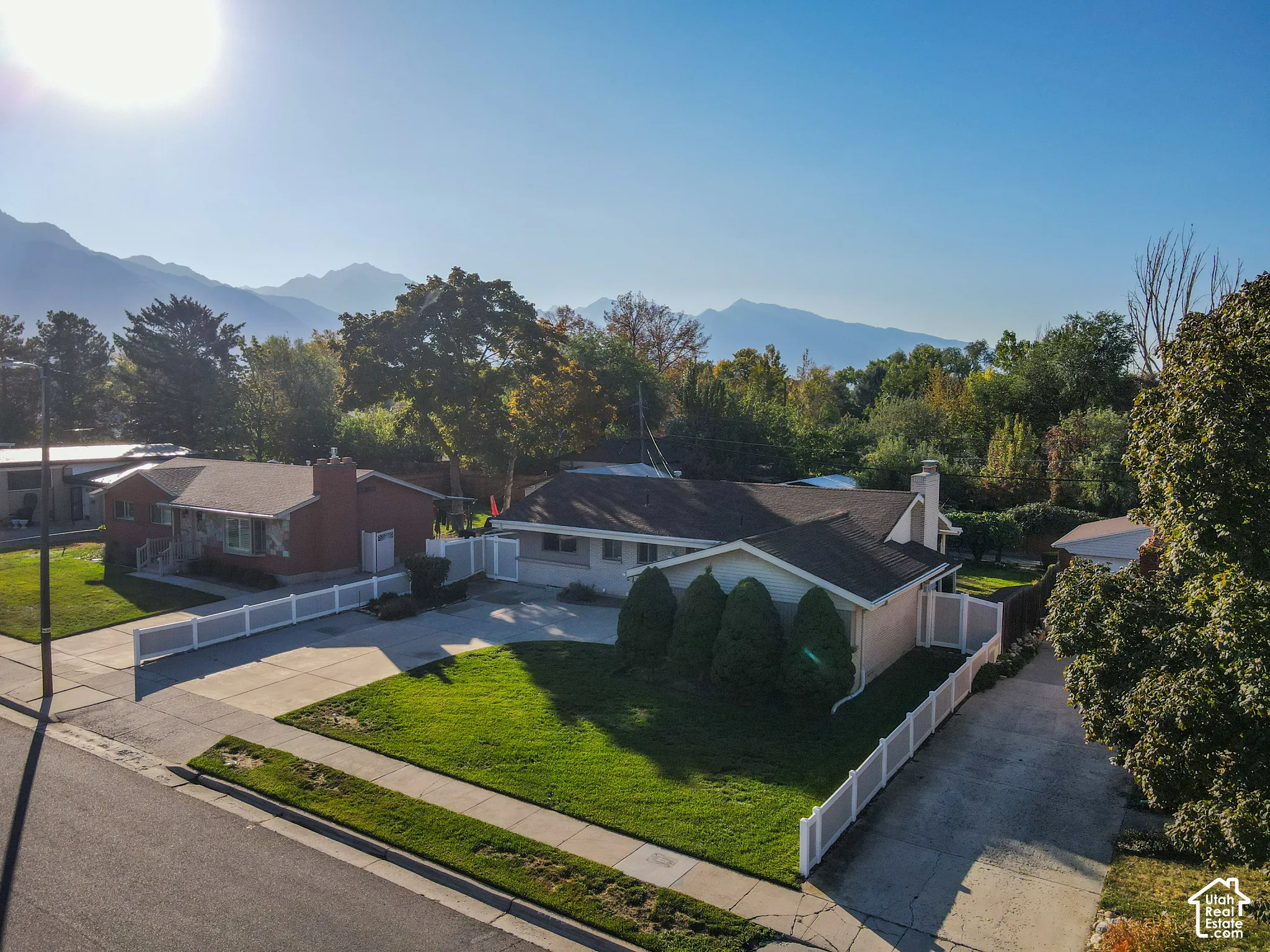 Mountain backdrop, mature trees, manicured lawn, paved driveway, white privacy fencing