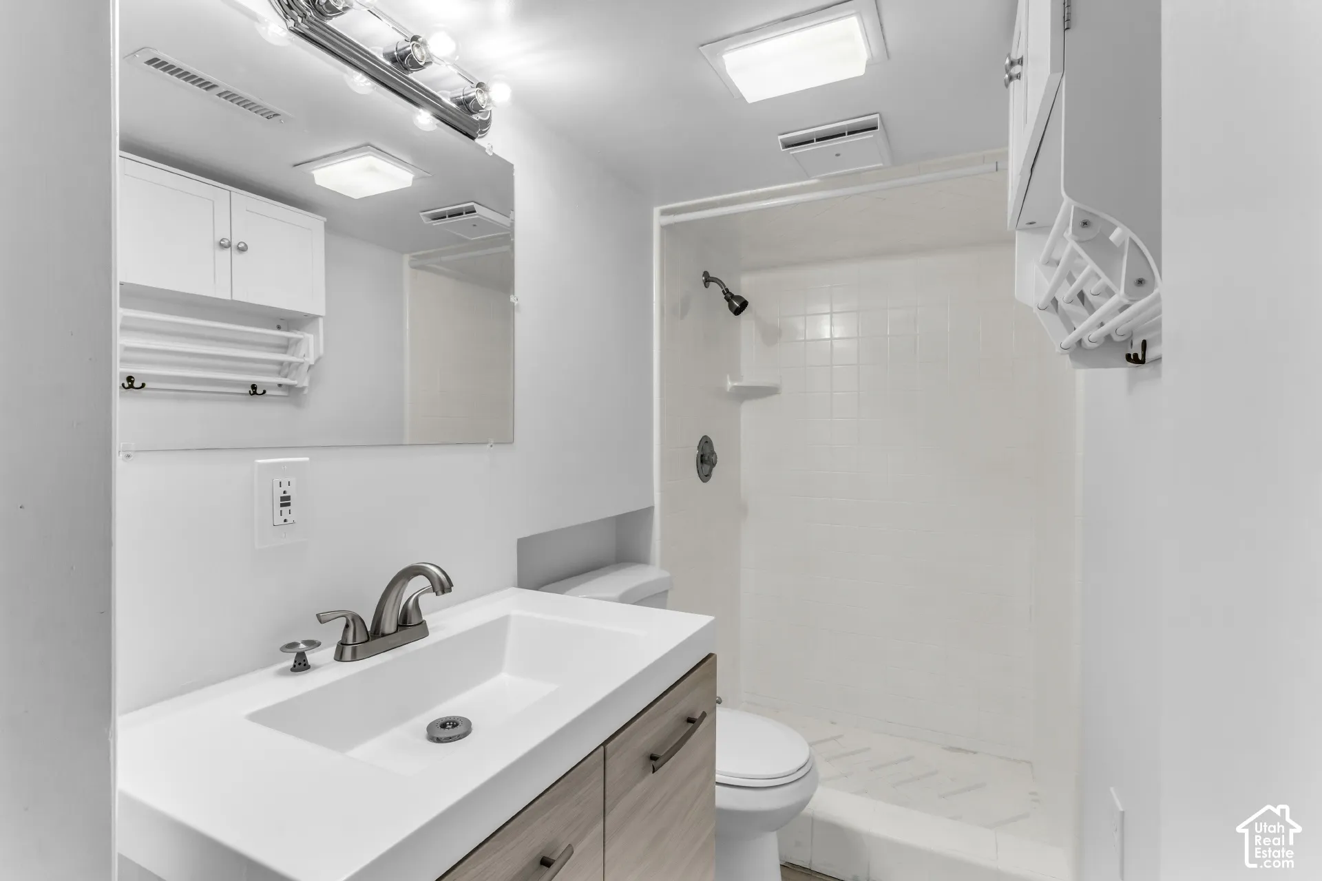 Modern bathroom featuring a floating wood-finish vanity with an integrated sink and quartz countertop, polished chrome faucet, framed mirror with integrated lighting, white subway tile surround in the walk-in shower with frameless glass enclosure, and rec