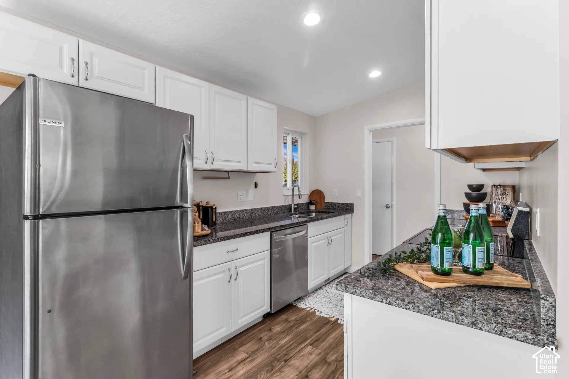 White cabinetry, stainless steel appliances, granite countertops, wood-finish flooring, and recessed lighting