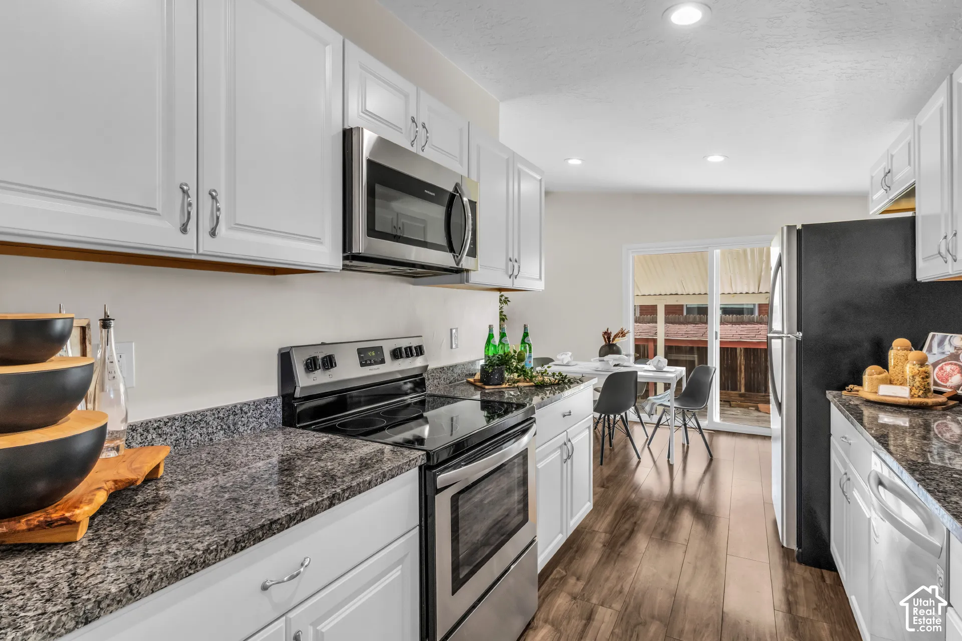 Kitchen featuring white cabinetry, granite-style countertops, stainless steel appliances, and wood-finish flooring