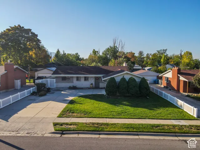 Single-story residence featuring a concrete driveway, a manicured lawn, and white privacy fencing