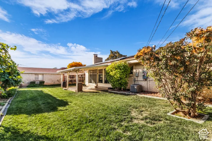Spacious backyard featuring a manicured lawn, mature landscaping with climbing vines, and a single-story residence with a covered porch entry