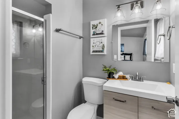 Glass-enclosed shower, single vanity with wood-finish cabinetry, rectangular undermount sink, wall-mounted light fixture, and a large mirror